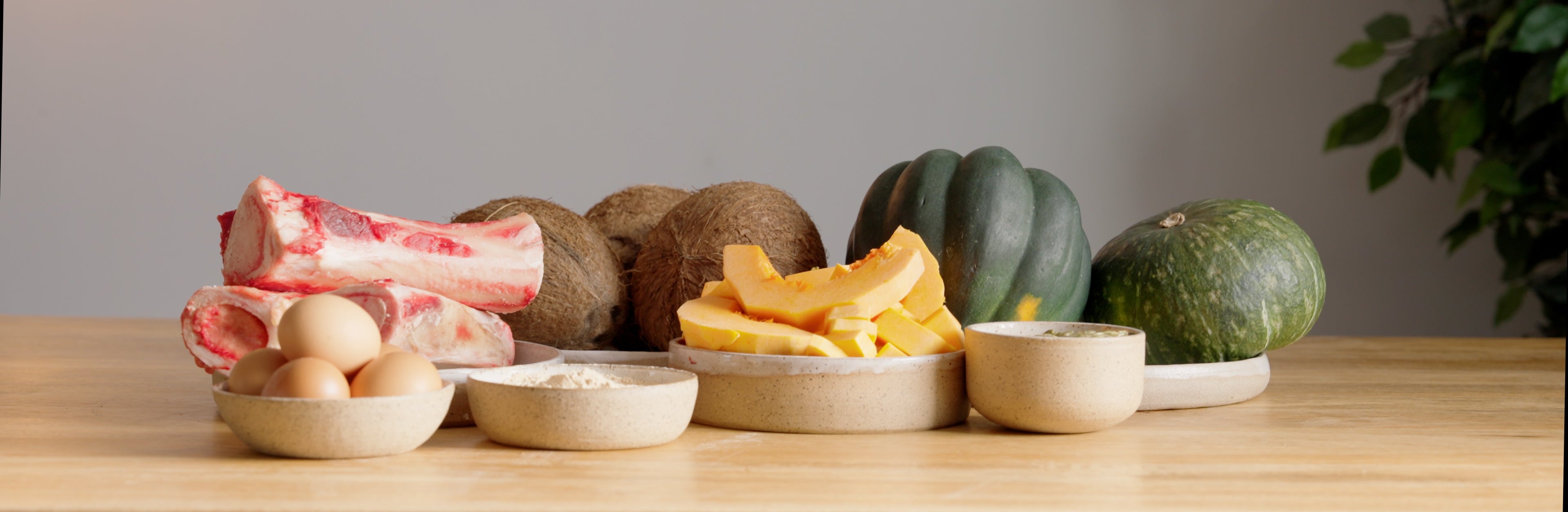 Assorted wholefood fruits and vegetables on a wooden table with a neutral background